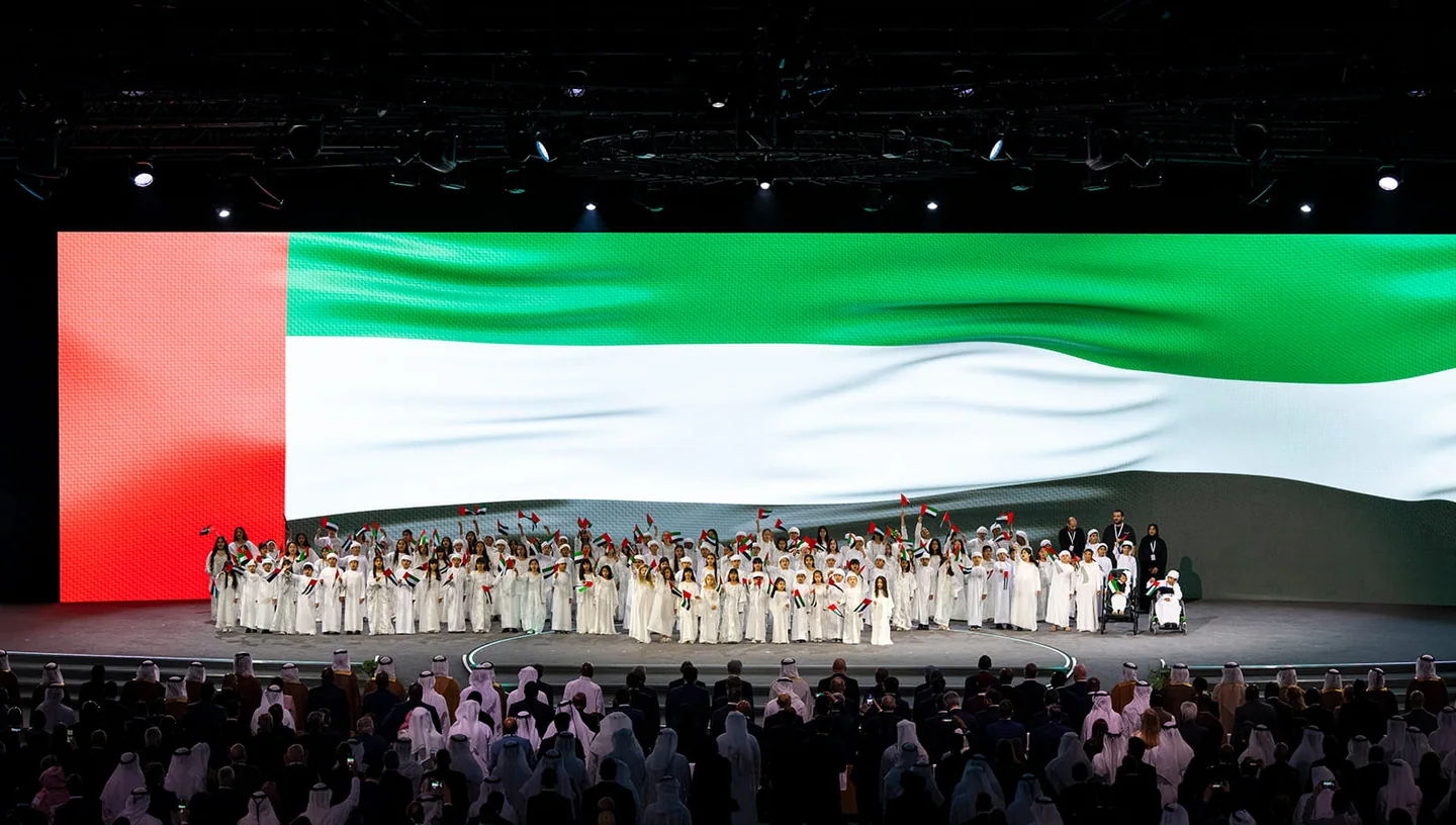 Ceremony participants in front of the UAE flag — Abu Dhabi Sustainability Week 2025. Archive photograph.