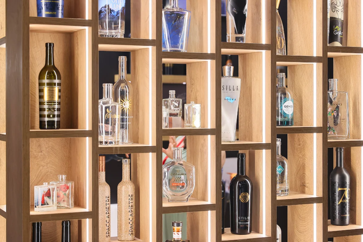 Des bouteilles de formes et de décors variés sur les étagères en bois d’un stand.