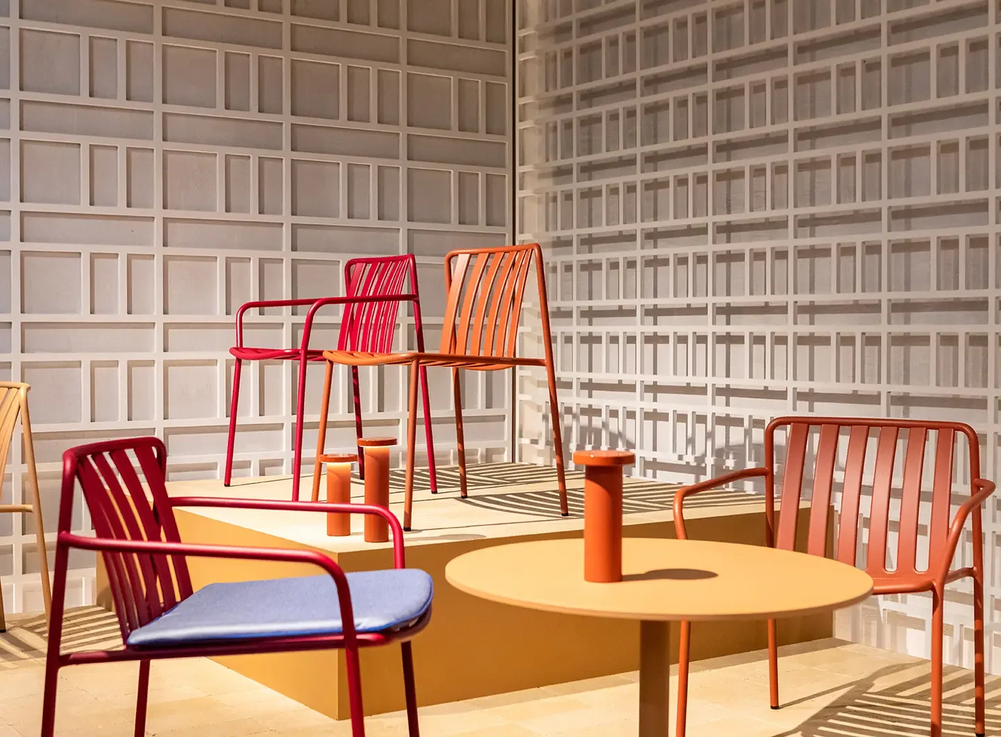 Ein orangefarbener Tisch und farbige Stühle in der Ausstellung von Pedrali.