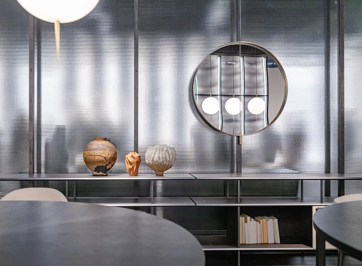 Ein runder Spiegel, ein Regal und Vasen in der Ausstellung von Living Divani.