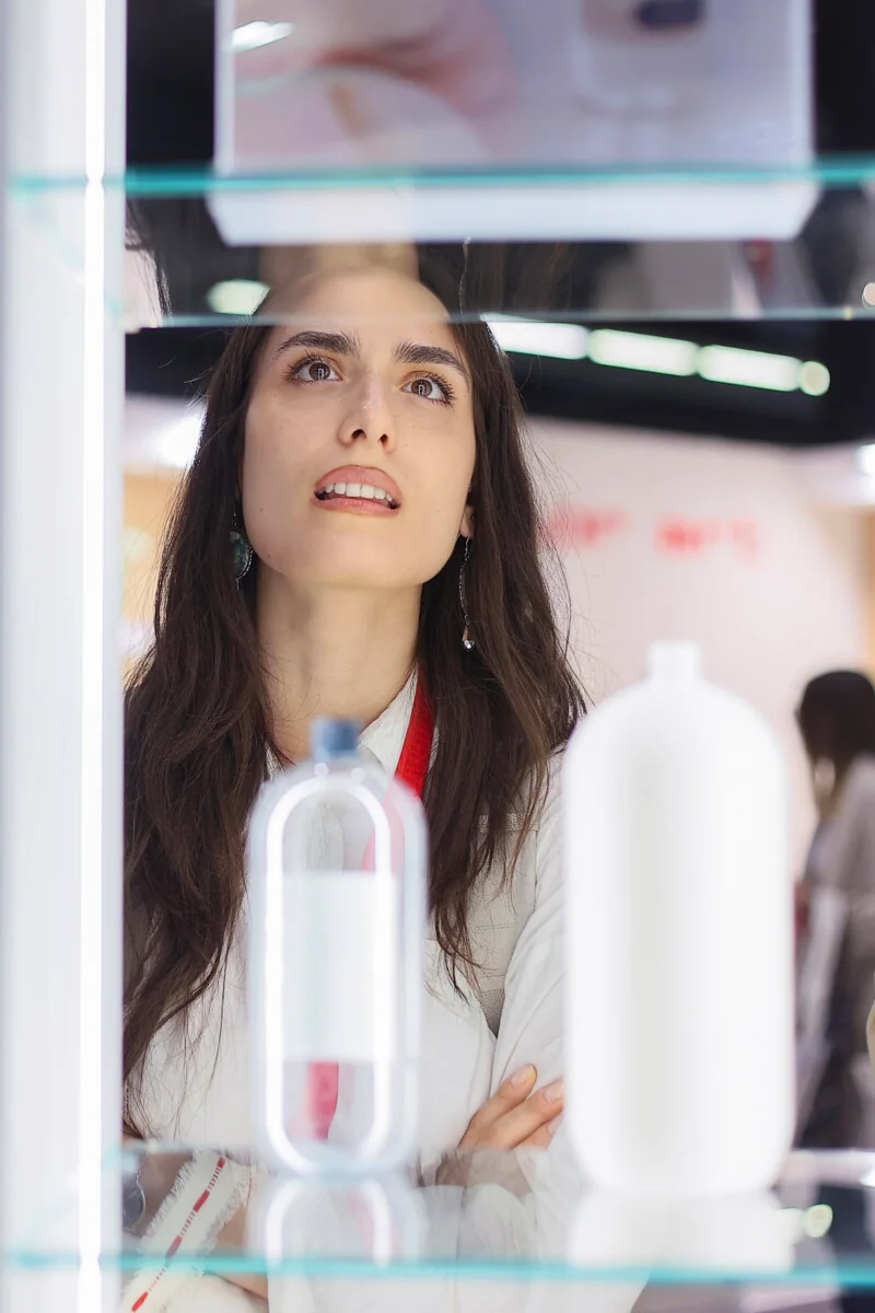 Une visiteuse regarde des flacons blancs dans une vitrine.