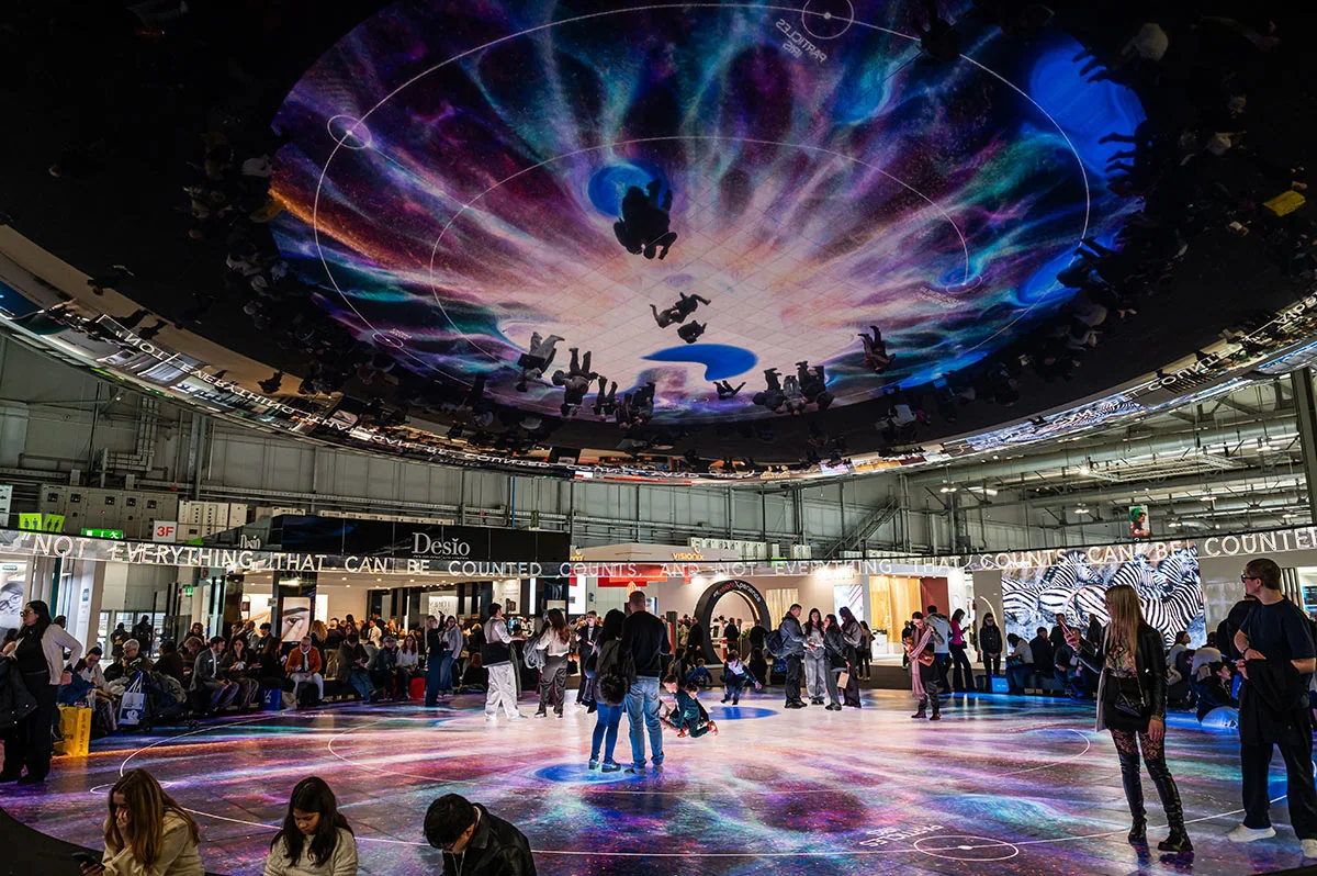 Un espacio expositivo con techo circular de espejos e iluminación de colores.