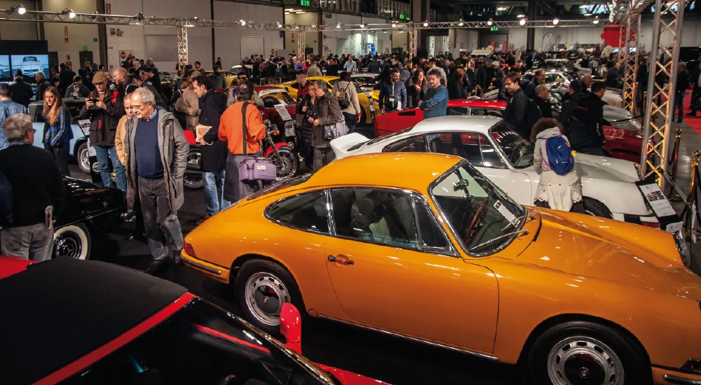 An orange classic sports car among exhibition visitors.