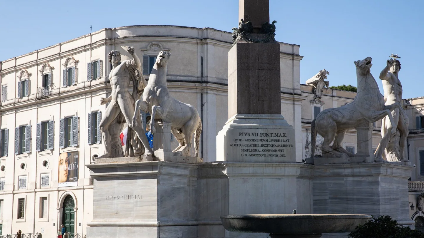 Scuderie del Quirinale în spatele sculpturilor din piață; vedere de arhivă cu afișul unei expoziții anterioare.